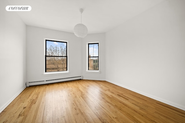 spare room with baseboards, a baseboard heating unit, light wood-style flooring, and visible vents