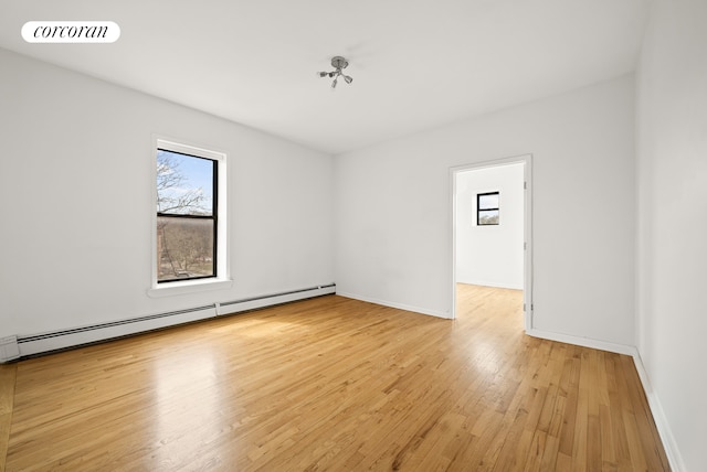 empty room featuring baseboards, light wood-style flooring, and a baseboard heating unit