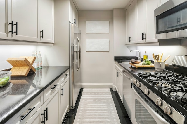 kitchen featuring appliances with stainless steel finishes, dark countertops, a sink, baseboards, and dark tile patterned flooring