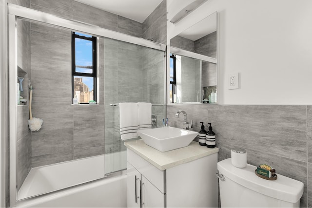 bathroom featuring vanity, combined bath / shower with glass door, toilet, and tile walls