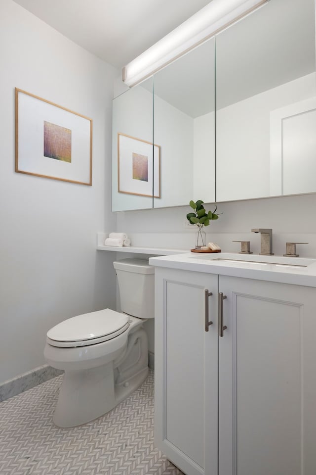 half bath with vanity, baseboards, and toilet