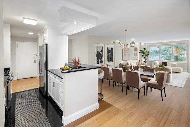 kitchen featuring freestanding refrigerator, white cabinetry, a notable chandelier, and dark countertops
