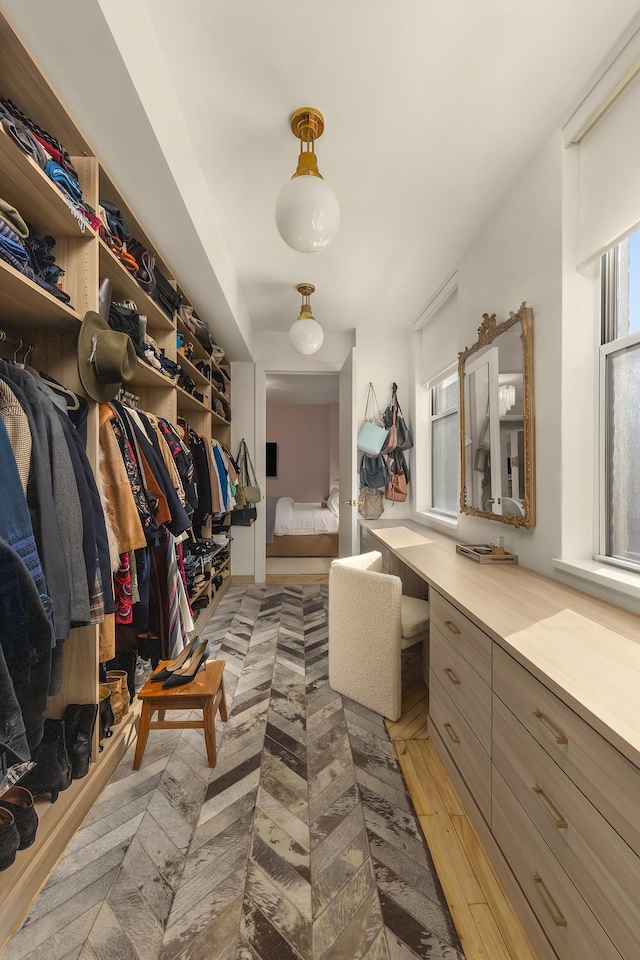 walk in closet featuring light wood finished floors and built in desk
