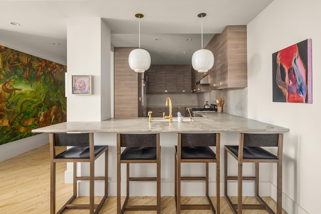 kitchen with a sink, a peninsula, light wood-type flooring, a kitchen bar, and modern cabinets