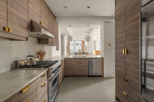 kitchen featuring pendant lighting, under cabinet range hood, brown cabinets, a sink, and premium appliances