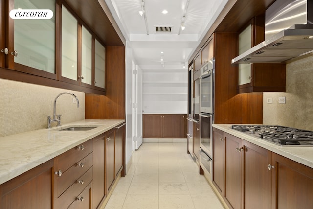 kitchen with wall chimney range hood, backsplash, visible vents, appliances with stainless steel finishes, and a sink