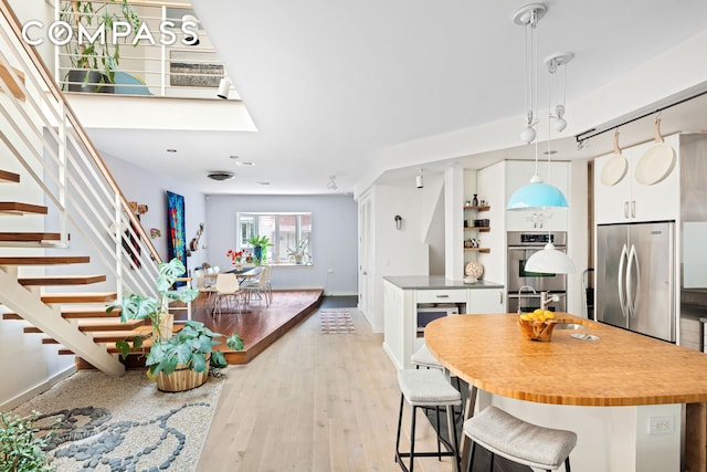 65 Jackson St, New York City, NY 11211 - kitchen with appliances with stainless steel finishes, white cabinetry, light wood-type flooring, hanging light fixtures, and a breakfast bar area