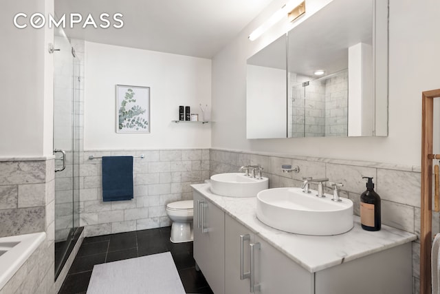 bathroom with double vanity, a sink, a stall shower, and tile walls