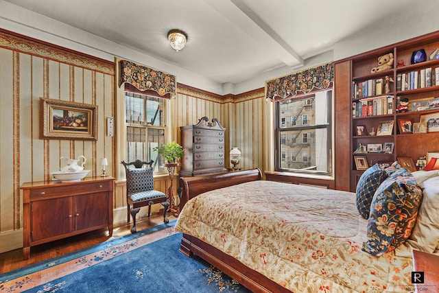 bedroom with beamed ceiling and wood finished floors