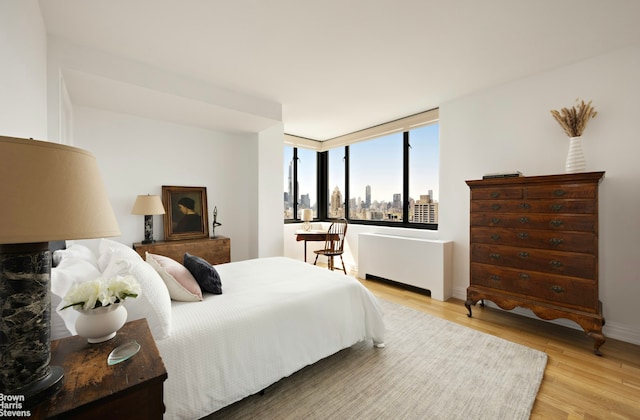 bedroom with baseboards, light wood finished floors, and radiator heating unit