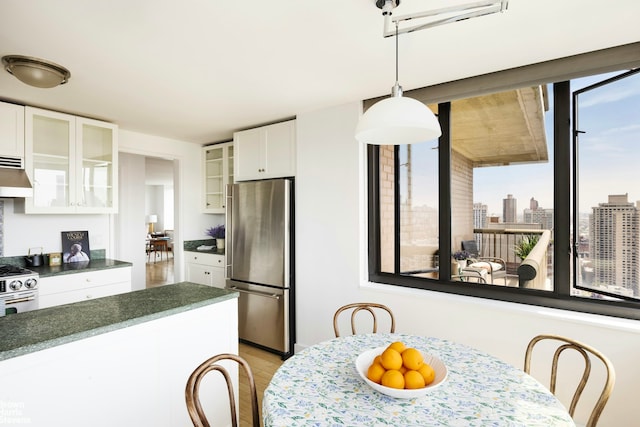 kitchen featuring dark countertops, appliances with stainless steel finishes, white cabinets, glass insert cabinets, and under cabinet range hood