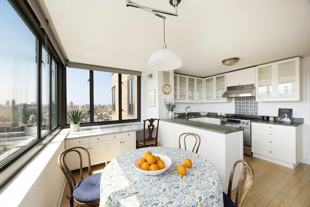 kitchen with dark countertops, white cabinetry, under cabinet range hood, stainless steel range with gas stovetop, and light wood finished floors