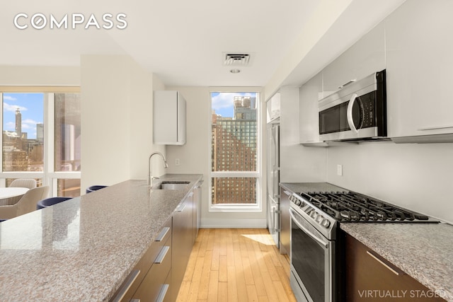 350 W 42nd St Unit 26G, New York City, NY 10036 - kitchen featuring stainless steel appliances, a skyline view, a sink, light wood-type flooring, and light stone counters