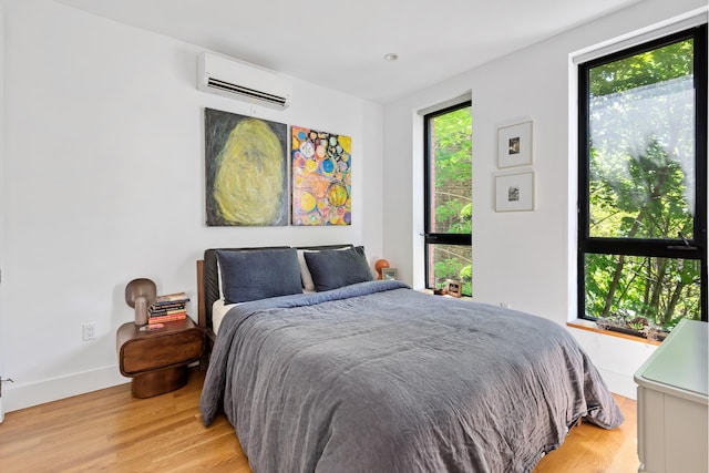 bedroom with light wood-type flooring, a wall mounted air conditioner, and baseboards