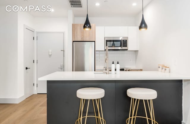 kitchen featuring a kitchen breakfast bar, appliances with stainless steel finishes, decorative backsplash, and light wood-type flooring