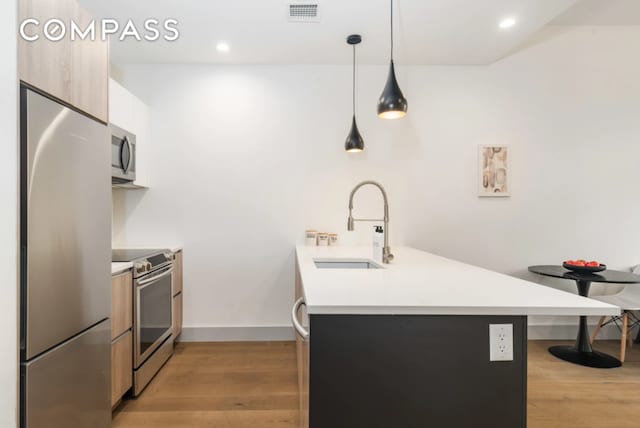 kitchen with a peninsula, modern cabinets, light countertops, a sink, and appliances with stainless steel finishes