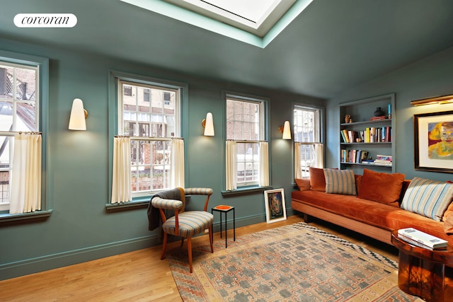 sitting room with wood finished floors, healthy amount of natural light, baseboards, vaulted ceiling, and built in features
