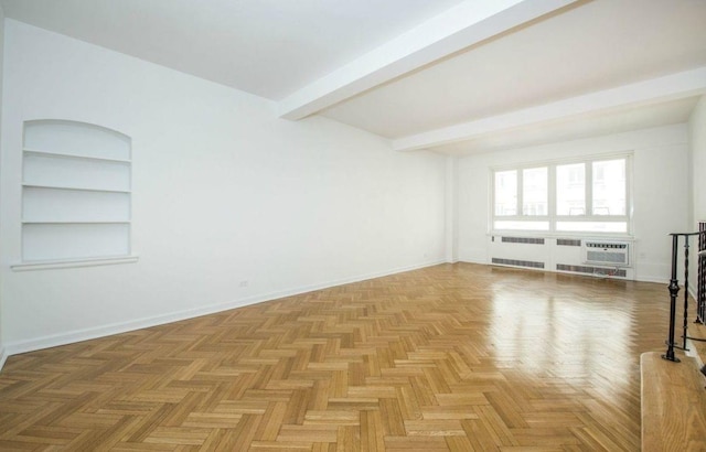 unfurnished living room featuring beamed ceiling, baseboards, a wall unit AC, and built in shelves