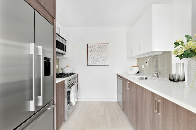 kitchen featuring appliances with stainless steel finishes, a sink, modern cabinets, tasteful backsplash, and light wood finished floors