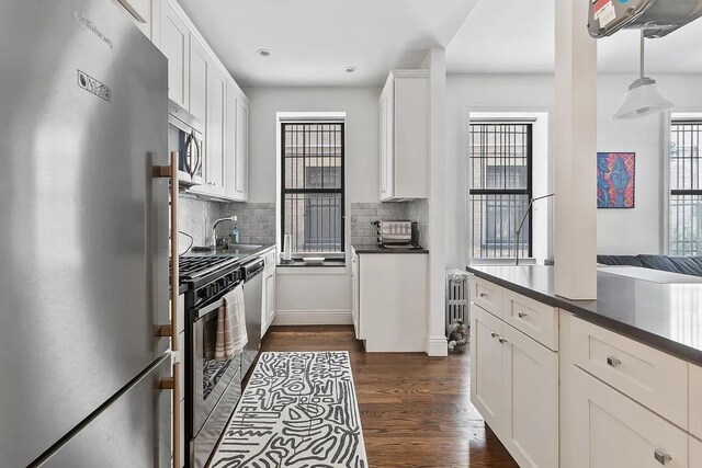 3117 Broadway Unit 1, New York City, NY 10027 - kitchen with appliances with stainless steel finishes, dark countertops, tasteful backsplash, dark wood finished floors, and white cabinets