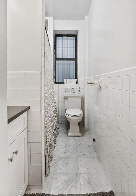 3117 Broadway Unit 1, New York City, NY 10027 - bathroom with tile walls, toilet, wainscoting, and a shower with shower curtain