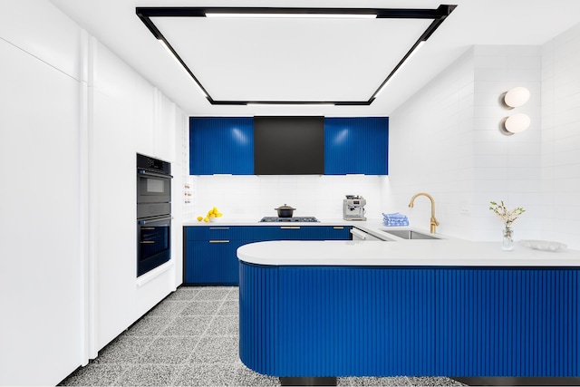 kitchen featuring a sink, blue cabinets, a peninsula, and light countertops