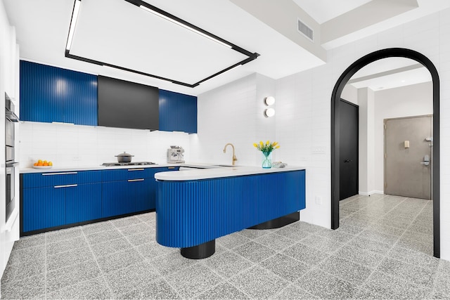 kitchen with blue cabinetry, arched walkways, light countertops, gas cooktop, and tile walls