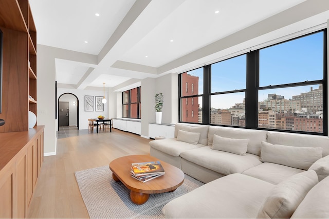 living area featuring light wood-type flooring, beam ceiling, coffered ceiling, arched walkways, and a view of city