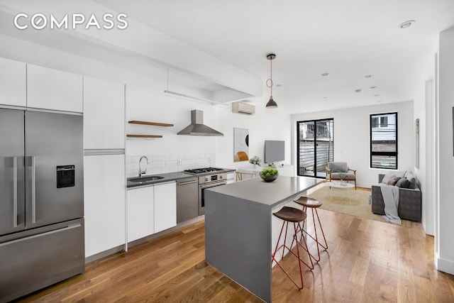 79 Clay St Unit 1R, New York City, NY 11222 - kitchen with appliances with stainless steel finishes, wall chimney exhaust hood, an AC wall unit, a sink, and white cabinets