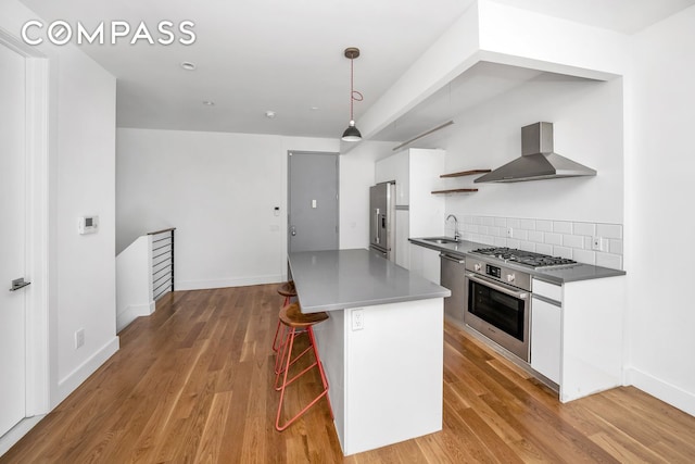 79 Clay St Unit 1R, New York City, NY 11222 - kitchen with wall chimney range hood, a sink, appliances with stainless steel finishes, white cabinetry, and light wood finished floors