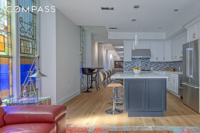 kitchen featuring high end refrigerator, light countertops, tasteful backsplash, exhaust hood, and white cabinetry