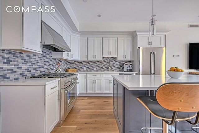 kitchen with premium appliances, wall chimney exhaust hood, light countertops, a breakfast bar, and light wood-style floors
