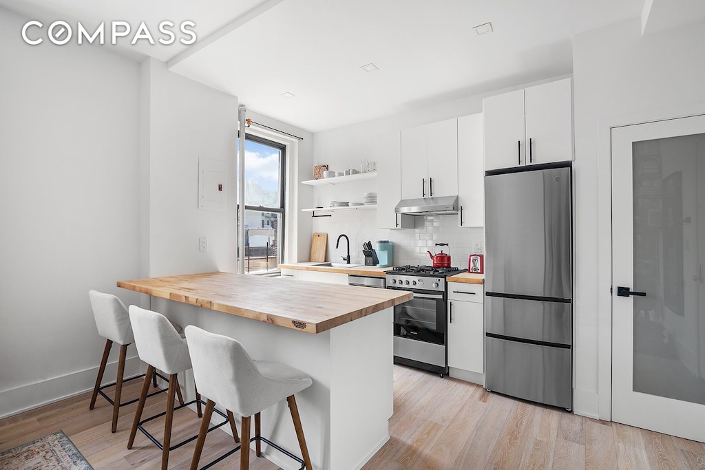 kitchen with stainless steel appliances, butcher block counters, a breakfast bar, a sink, and light wood-style floors