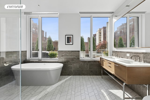 bathroom featuring double vanity, tile walls, plenty of natural light, and a freestanding bath
