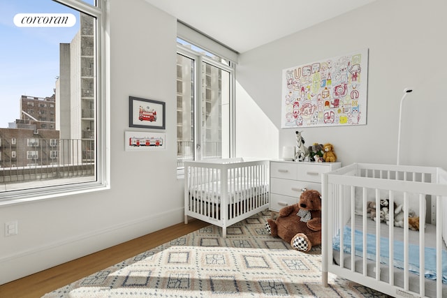 bedroom with baseboards, a crib, wood finished floors, and multiple windows