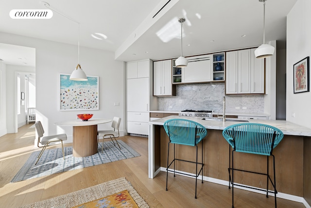 kitchen featuring a sink, light wood-style flooring, backsplash, and white cabinetry