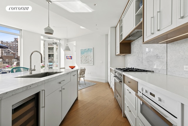 kitchen featuring beverage cooler, baseboards, tasteful backsplash, a sink, and light wood-style flooring