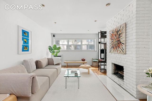living area featuring brick wall, a brick fireplace, and wood finished floors