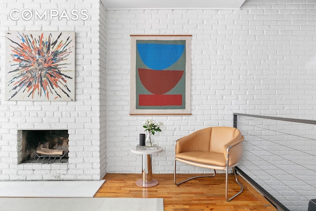 sitting room with a brick fireplace, wood finished floors, and brick wall