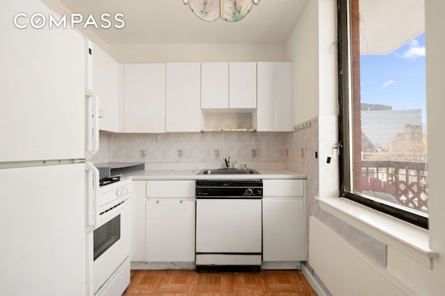 kitchen with white appliances, a sink, white cabinetry, and light countertops