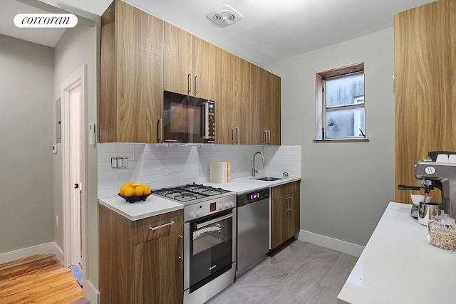 kitchen with appliances with stainless steel finishes, a sink, light countertops, tasteful backsplash, and visible vents