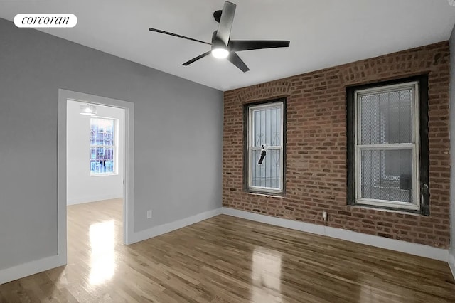empty room with ceiling fan, brick wall, baseboards, wood finished floors, and visible vents