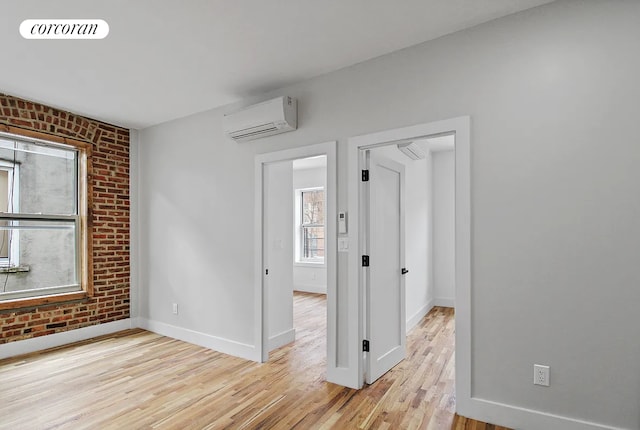 empty room with an AC wall unit, baseboards, light wood finished floors, and brick wall