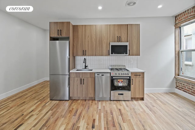 kitchen featuring light wood-type flooring, a sink, baseboards, light countertops, and stainless steel appliances