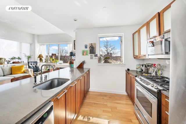 kitchen with light wood-style floors, baseboards, brown cabinets, a sink, and stainless steel appliances