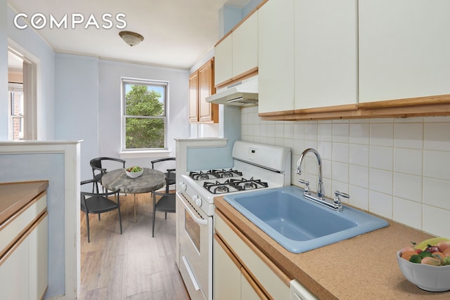 kitchen with a sink, light countertops, under cabinet range hood, white gas range oven, and backsplash