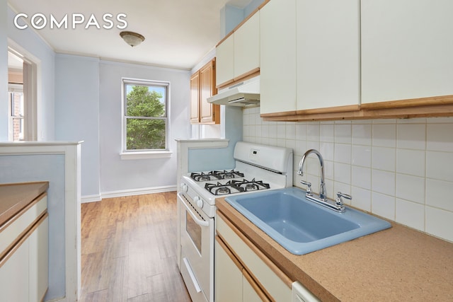 kitchen with decorative backsplash, a sink, light countertops, white range with gas cooktop, and under cabinet range hood
