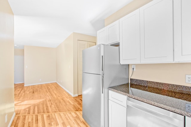 kitchen featuring white dishwasher, white cabinets, freestanding refrigerator, light wood-style floors, and dark stone counters