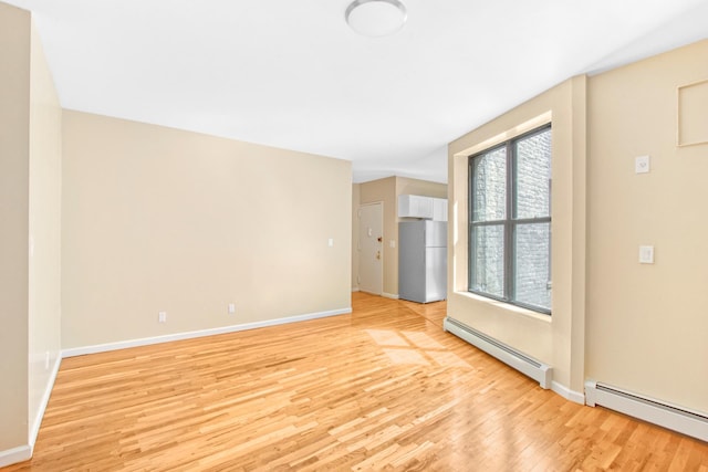empty room featuring baseboards, light wood-style flooring, and a baseboard heating unit