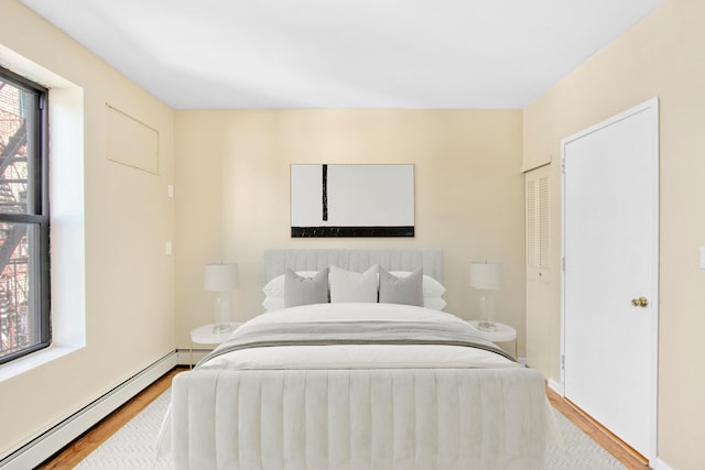 bedroom with baseboards, a baseboard radiator, a closet, and wood finished floors